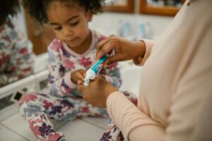 A parent handing their child a toothbrush with toothpaste on it.